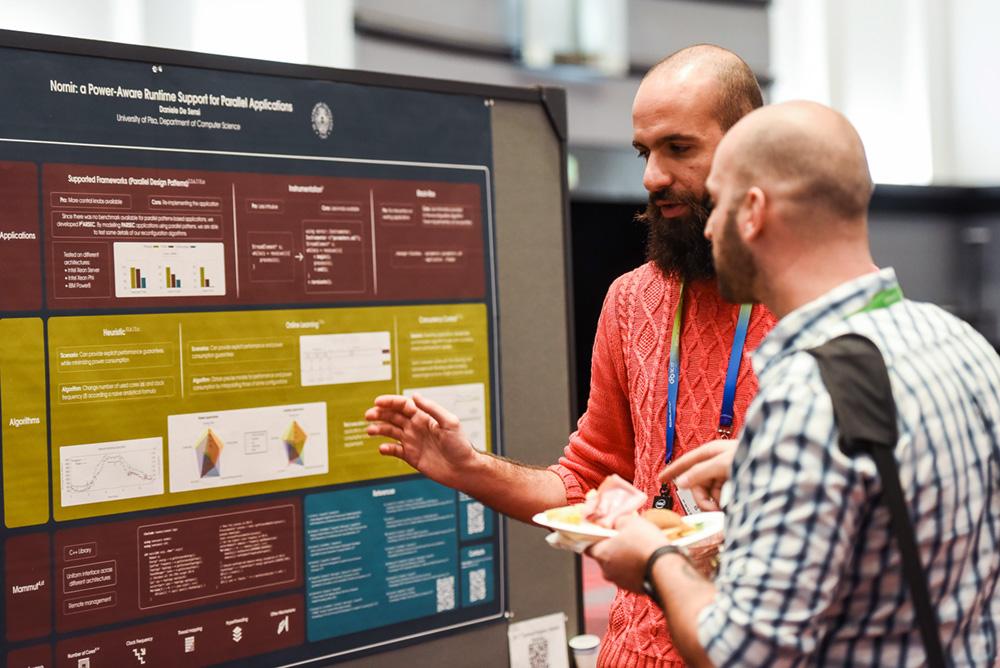 Man with a beard presents a poster, while another man listens.