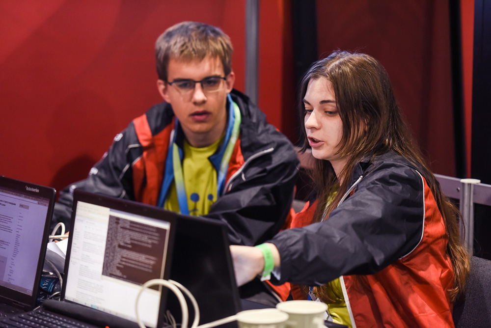 Woman points to her laptop while teaching a man something.
